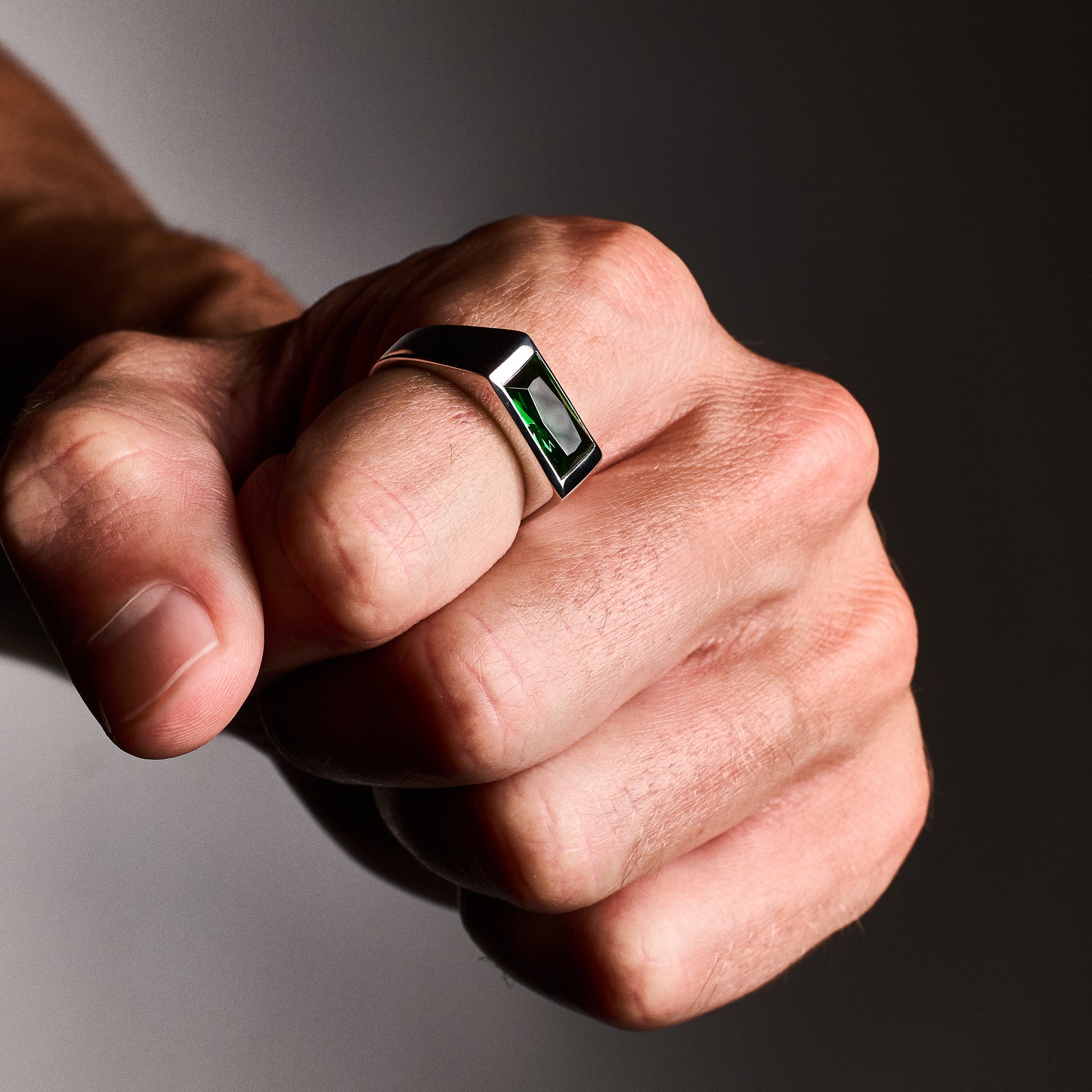 Close-up of a person wearing the Emerald Signet Ring with a green baguette-cut glass stone set in rhodium-plated sterling silver.